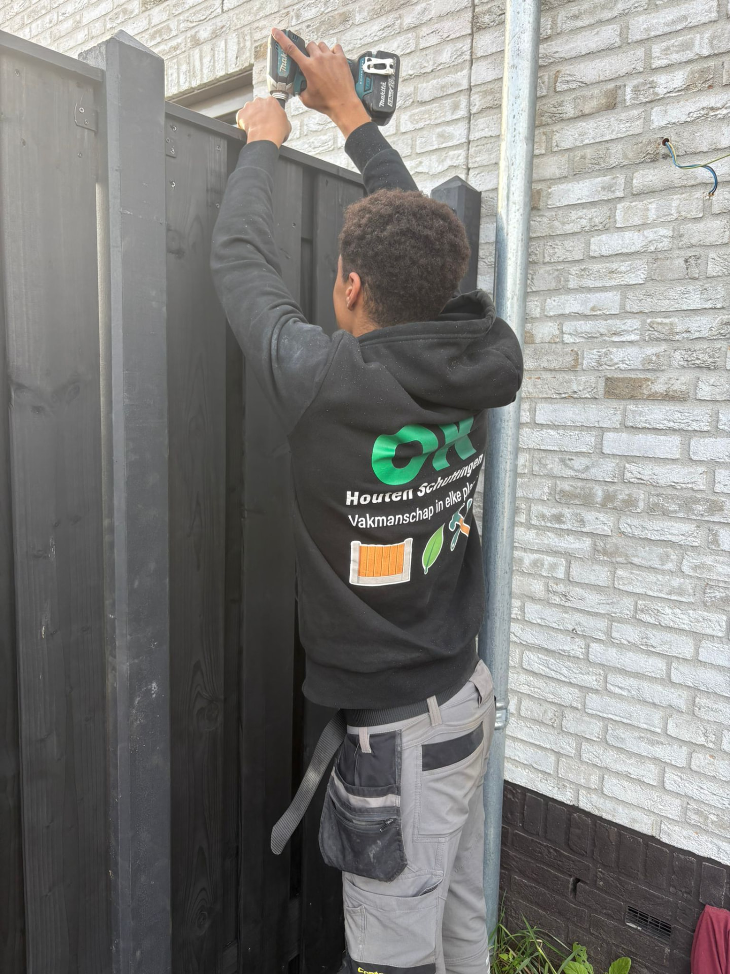 Monteur van OK Houten Schuttingen plaatst een antraciet gespoten schutting